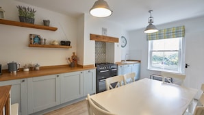 A kitchen with light grey cabinets, a wooden countertop, a stove, a sink, and a dining table with chairs. - Adventure House (Whitby)