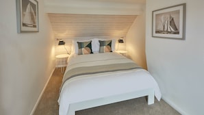 A bedroom with a bed, two bedside tables, a ceiling light, and two framed pictures on the walls. - Adventure House (Whitby)
