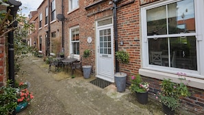 A brick building with a white door, a small patio with a table and chairs, and potted plants. - Adventure House (Whitby)
