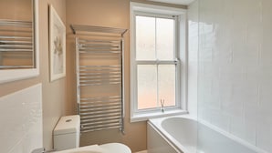 A bathroom with a toilet, a towel rack, a window, and a bathtub. - Adventure House (Whitby)