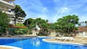 A swimming pool with lounge chairs, surrounded by trees and buildings. - Quiet apartment near the sea (Salou)