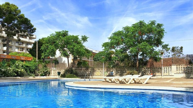 A swimming pool with lounge chairs, surrounded by trees and a fence. - Quiet apartment near the sea (Salou)
