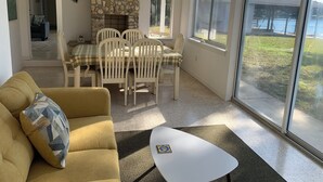 A cozy living room with a stone fireplace, a dining area with a checkered tablecloth, and large windows offering a view of a body of water. - Beautiful Indian Lake with canal leading to Crystal River and the Ocean. (Crystal River)