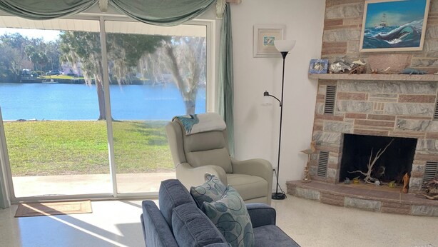 A living room with a grey sofa, a beige armchair, a fireplace, and a view of a lake through a sliding glass door. - Beautiful Indian Lake with canal leading to Crystal River and the Ocean. (Crystal River)