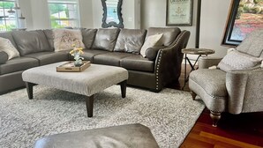 A living room with a brown leather sofa, a grey armchair, a patterned rug, and a small side table. - Enchanting 3 BR, minutes from Winerys, Snow Sking, exhilarating Rafting Tours. (Medford)