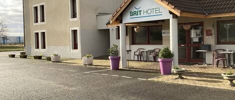 A building with a sign reading "BRIT HOTEL" and a smaller sign below it. There are outdoor seating areas with tables and chairs.