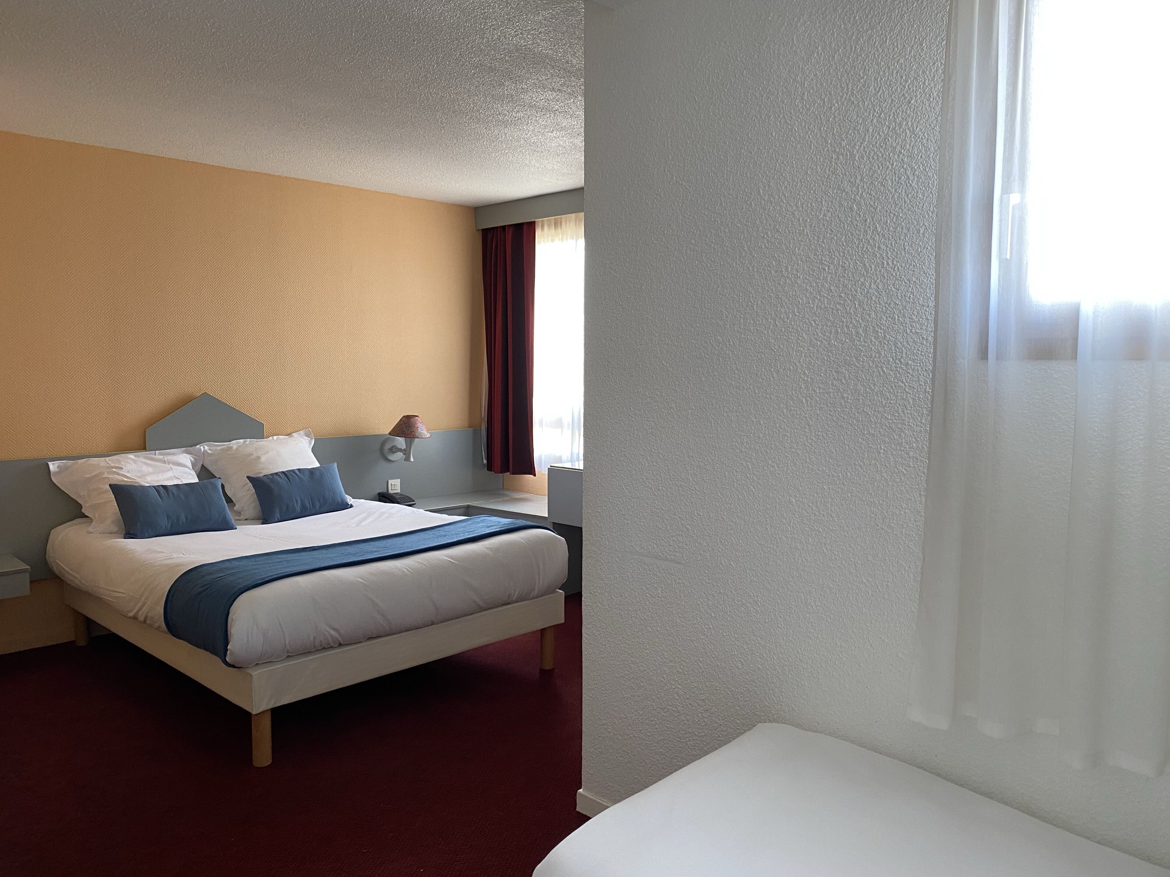 Ein Hotelzimmer mit einem Bett, einem Nachttisch, einer Lampe und einem Fenster mit Vorhängen.