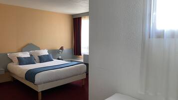 A hotel room with a bed, a nightstand, a lamp, and a window with curtains.