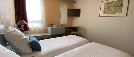 Habitación de hotel con dos camas, un escritorio, una silla, un televisor y un cuadro en la pared.