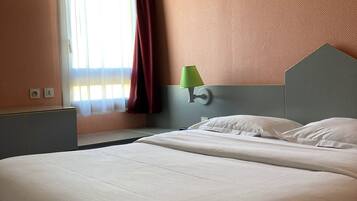 A hotel room with a large bed, a nightstand, a lamp, and a window with curtains.