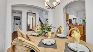 Un coin repas avec une table en bois dressée pour quatre personnes, un lustre et un escalier en arrière-plan.