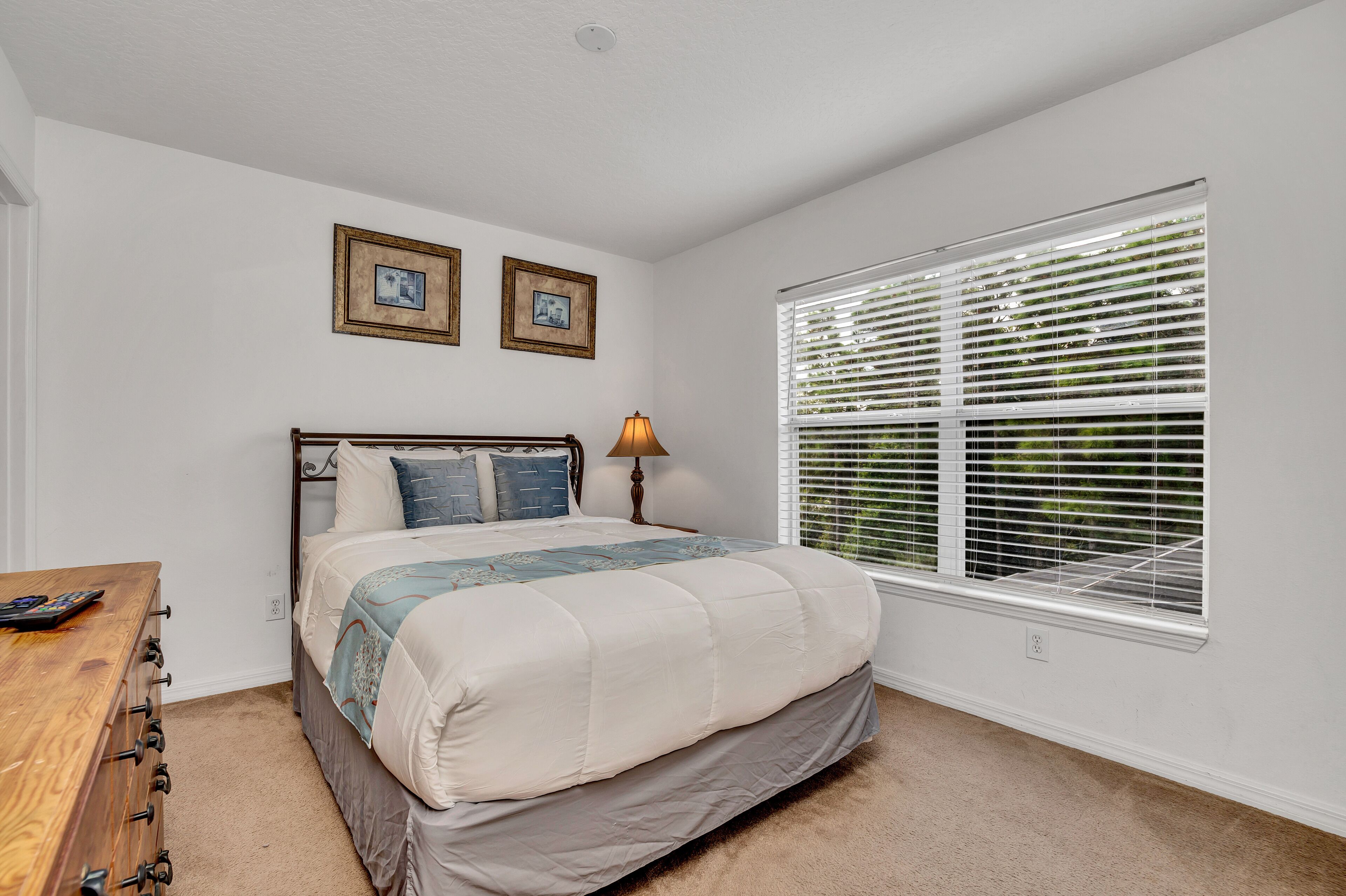 A bedroom with a bed, a nightstand, a lamp, and a window with blinds.