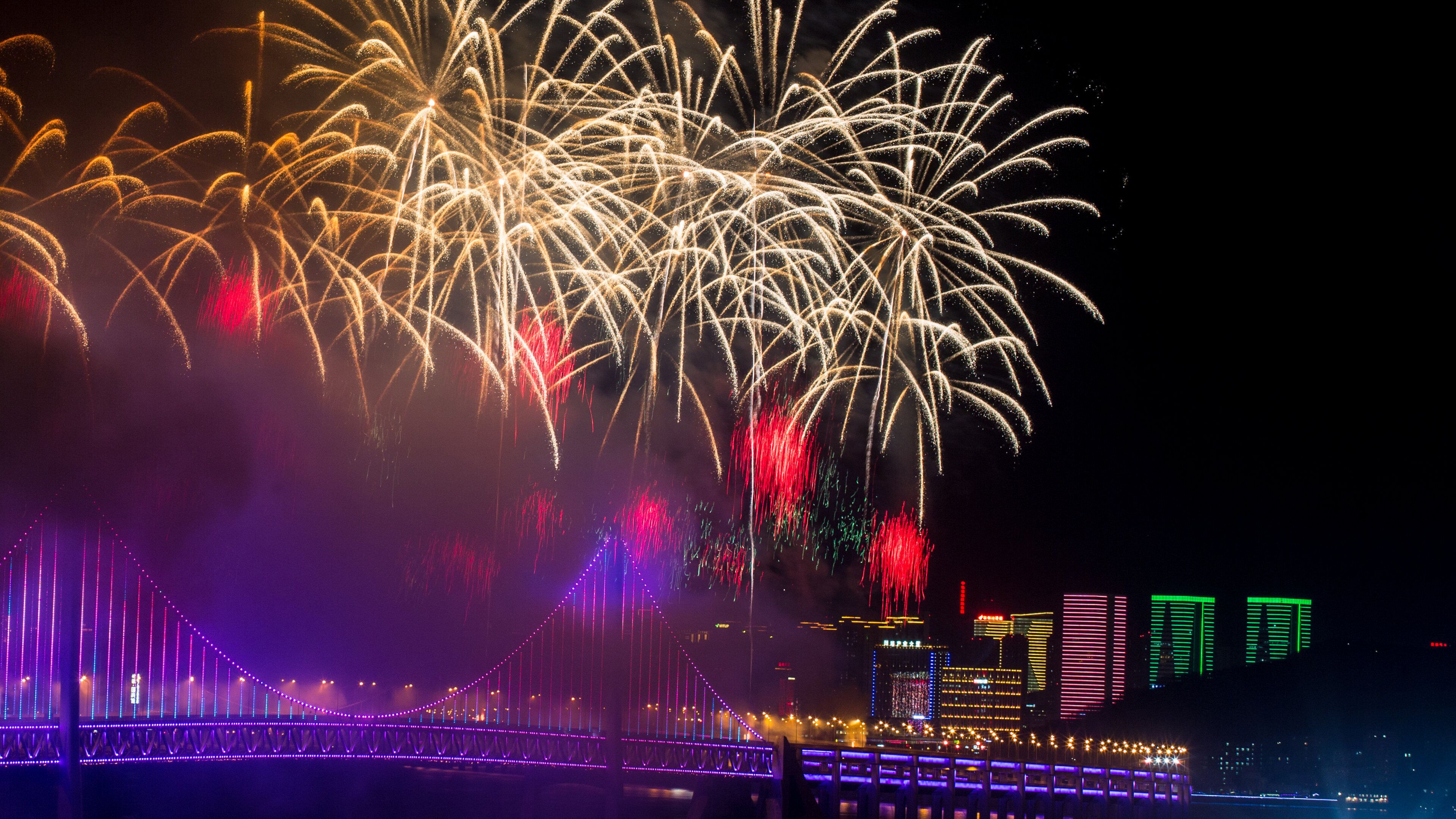 A bridge with illuminated lights and fireworks in the background.