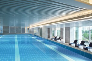 Una amplia piscina interior con baldosas azules brillantes, un diseño moderno en el techo y sillones de descanso junto a las ventanas.
