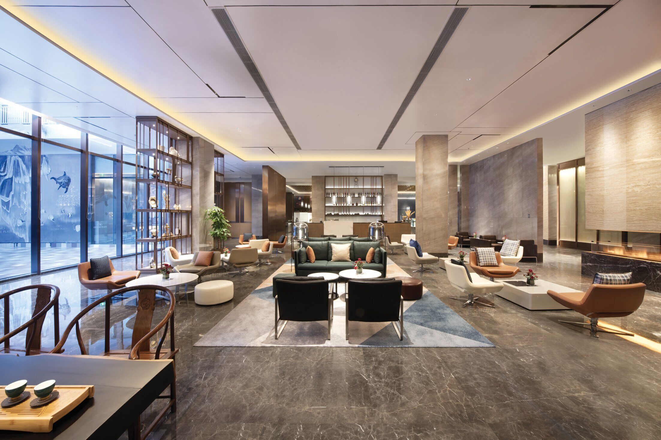 A modern hotel lobby with a central seating area, a bar, and a large window with a view.