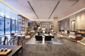 A modern hotel lobby with a central seating area, a bar, and a large window with a view.