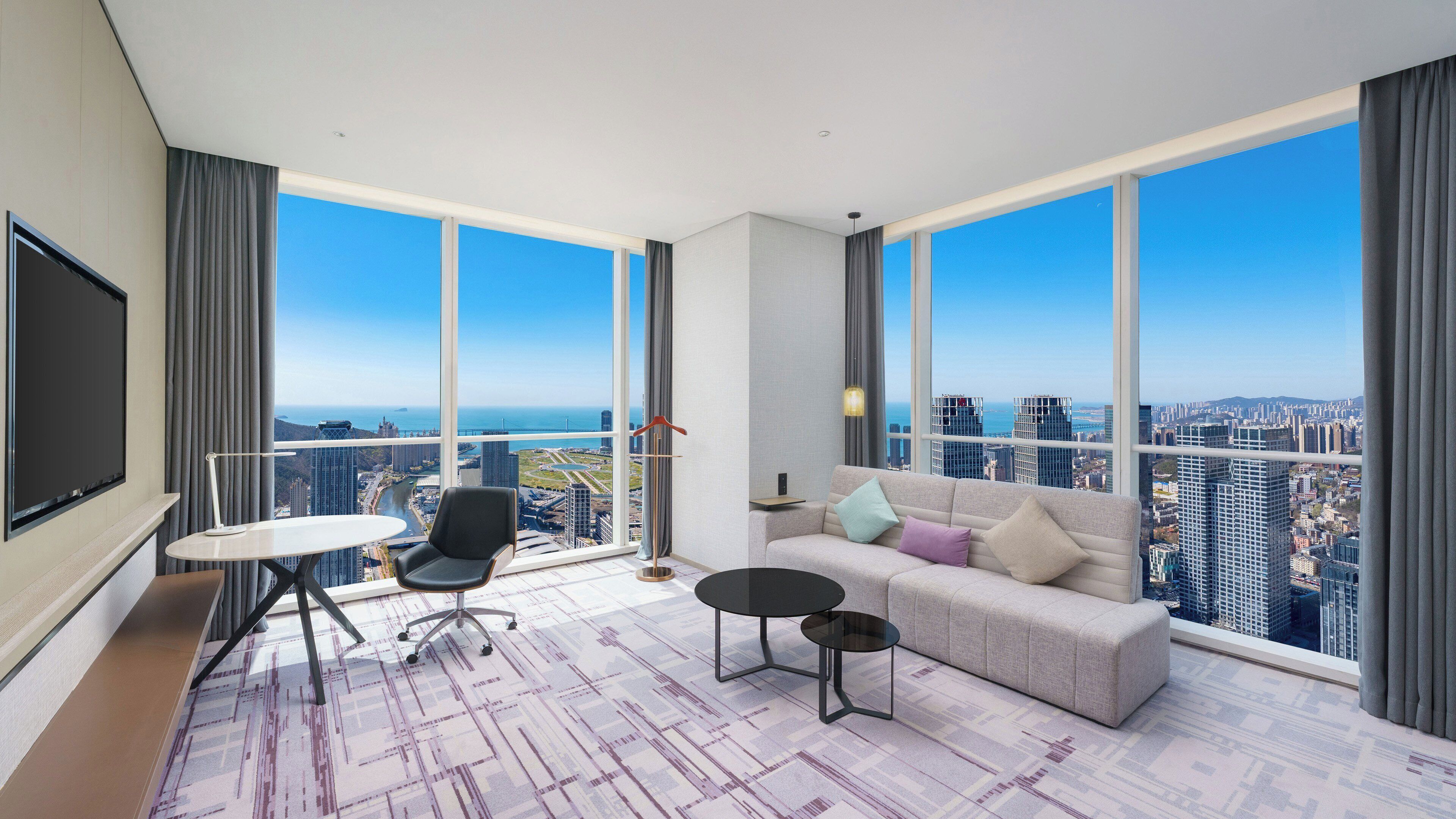Una sala de estar moderna con un sofá grande, una mesita y una silla. Tiene un ventanal con vistas a la ciudad.
