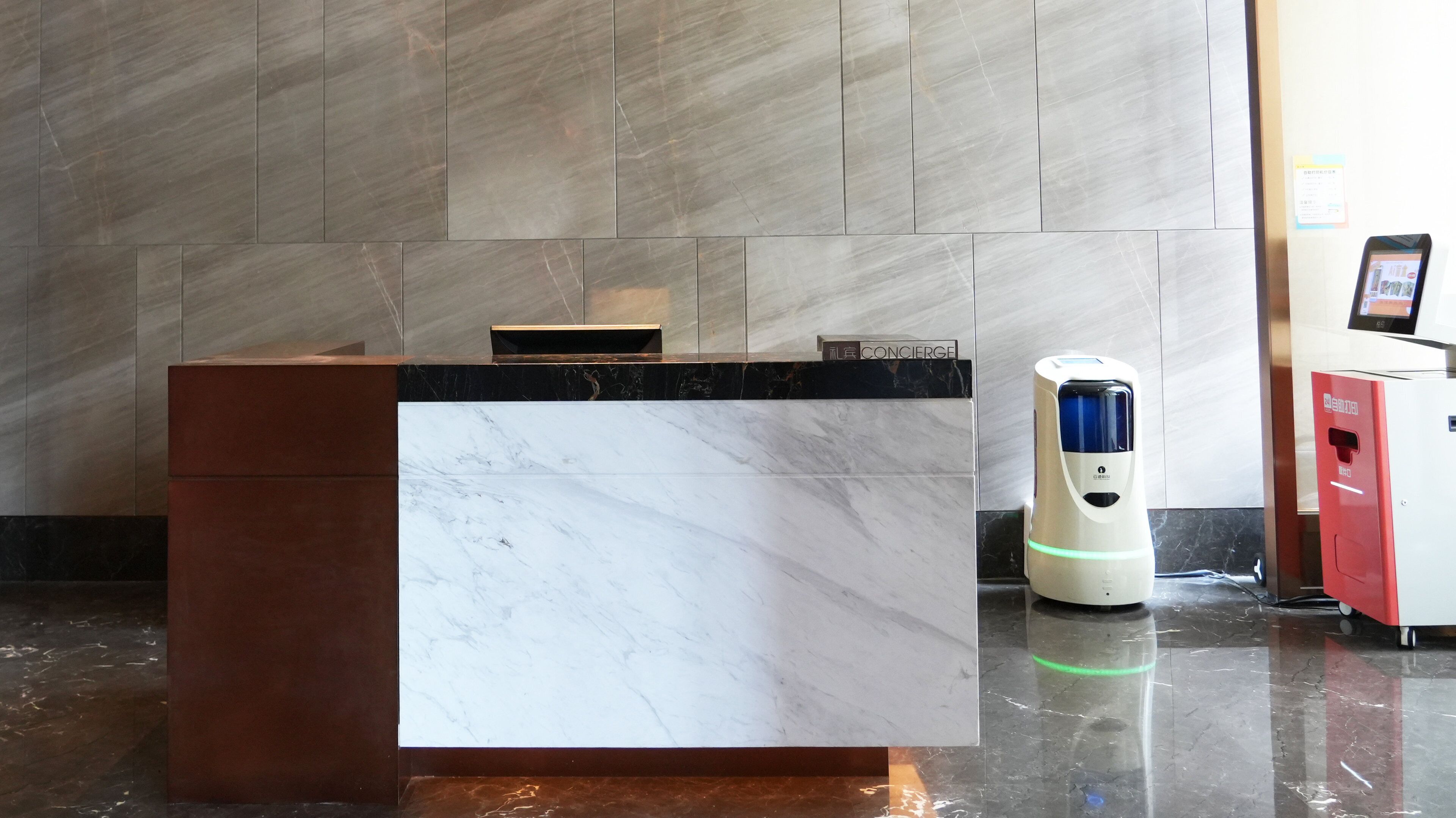 A reception desk with a marble top, a digital kiosk, and a red vending machine.