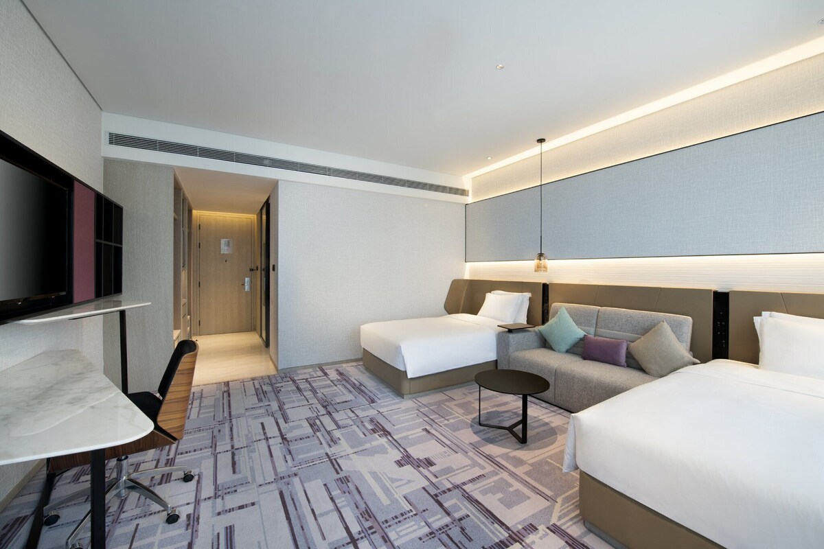 A hotel room with a bed, a sofa, a desk, and a TV.