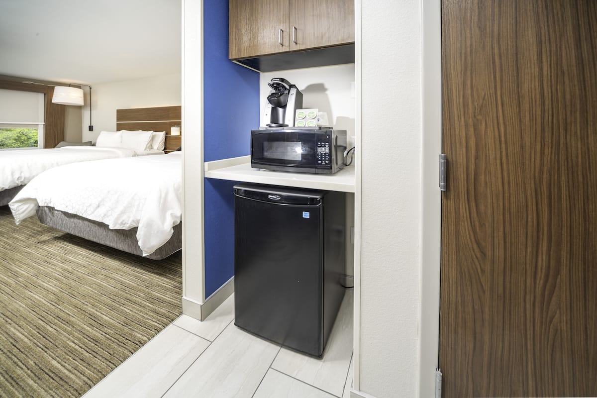 A hotel room with a kitchenette, including a microwave and a dishwasher. There are two beds with white bedding and a blue accent wall.