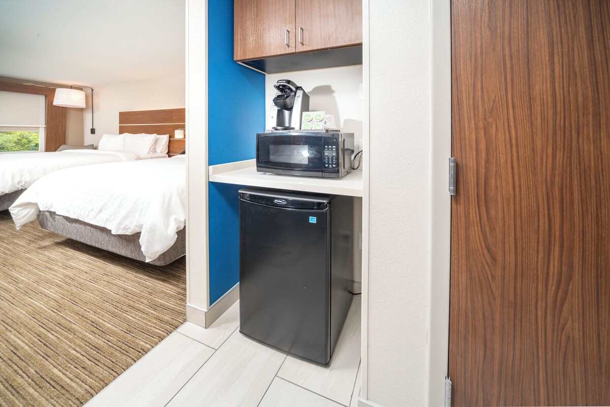 Hotelkamer met kitchenette, inclusief een magnetron en vaatwasser. Er zijn twee bedden met wit beddengoed en een blauwe accentmuur.