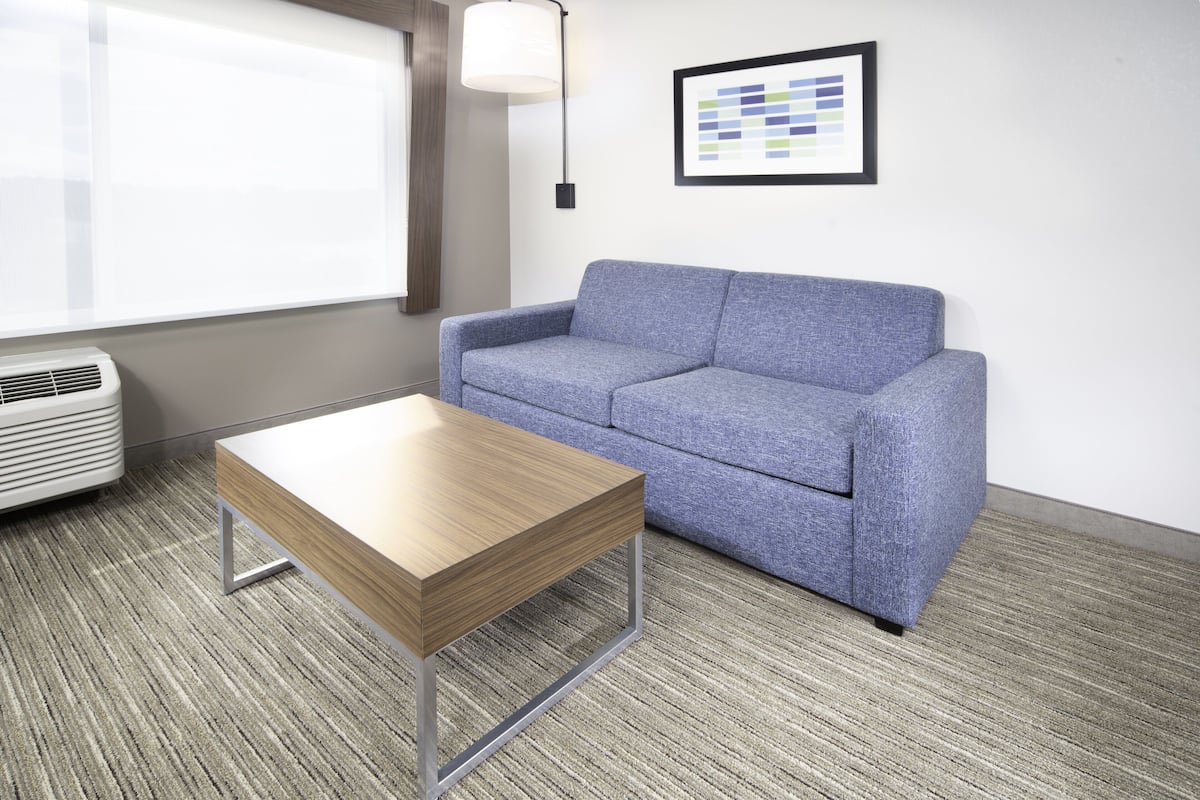 A room with a grey sofa, a wooden coffee table, a white air conditioner, and a framed color palette on the wall.