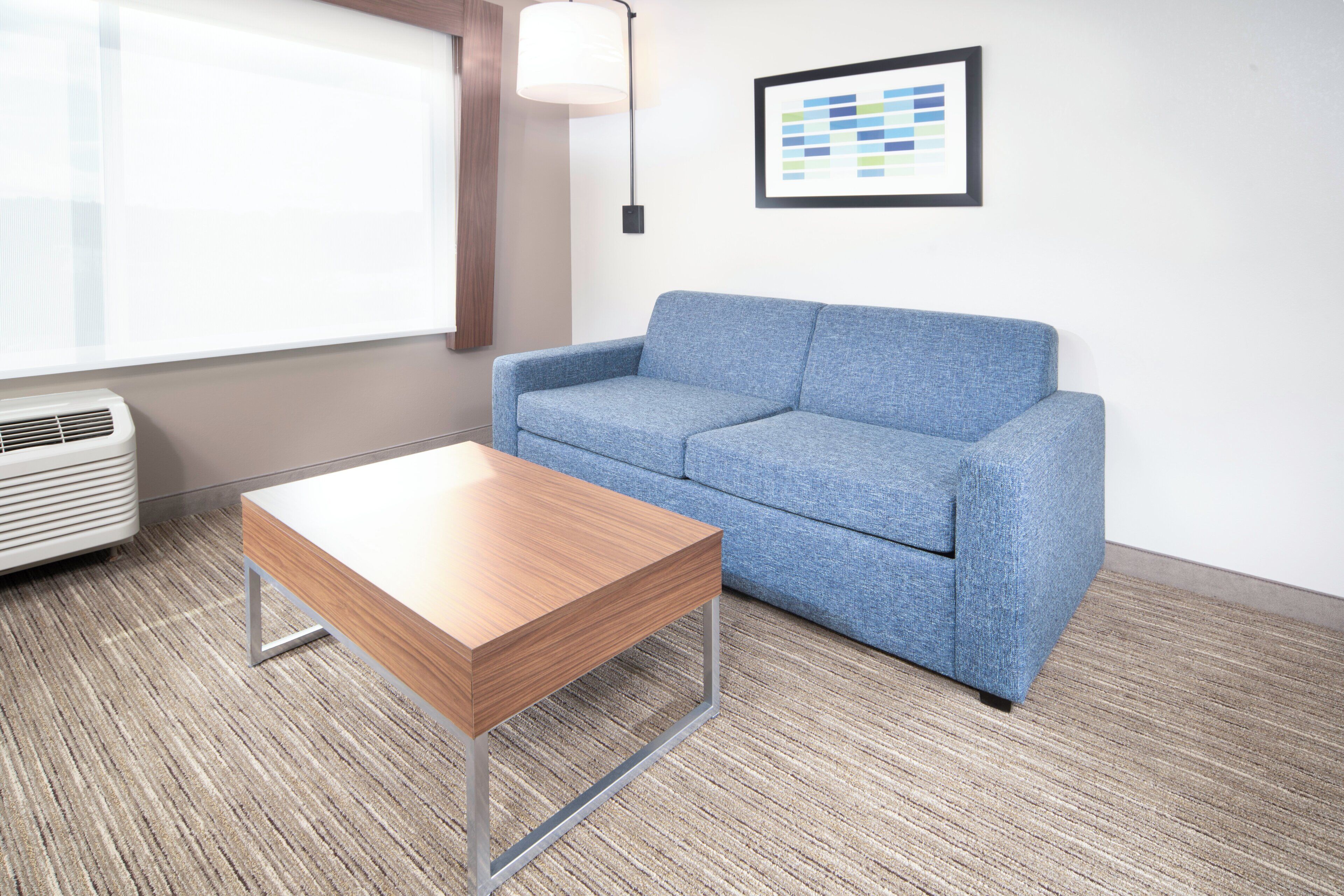 A room with a blue sofa, a wooden coffee table, a wall-mounted lamp, and a framed chart.