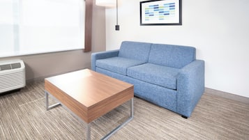 A room with a blue sofa, a wooden coffee table, a wall-mounted lamp, and a framed chart.