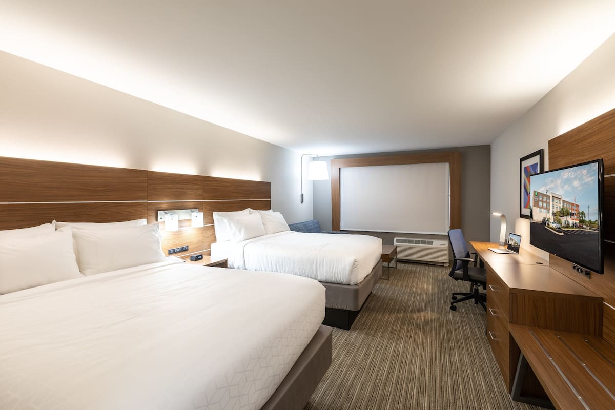 A hotel room with two beds, a desk with a computer, a TV, and a large window.