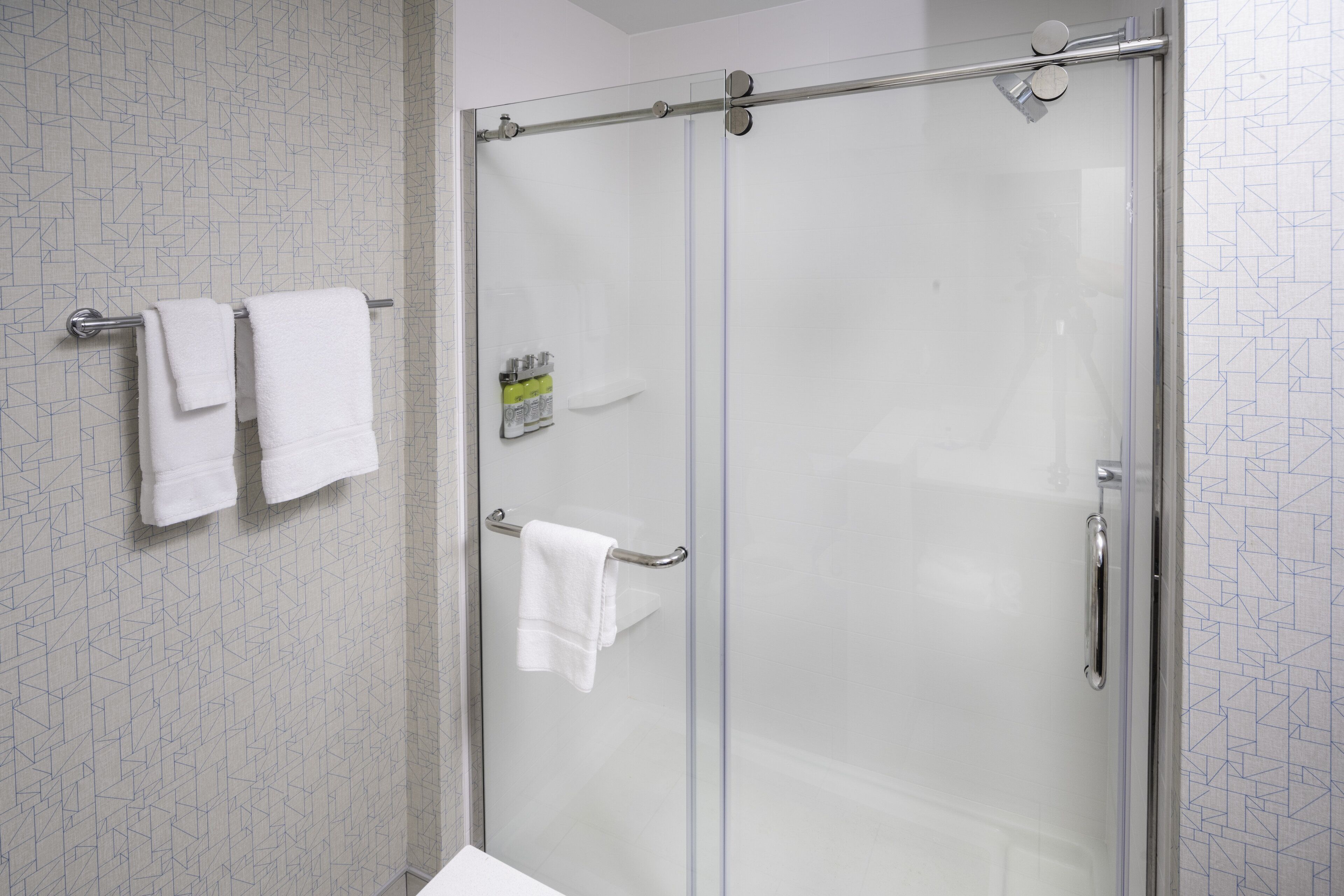 A glass-enclosed shower with a towel rack holding two white towels.