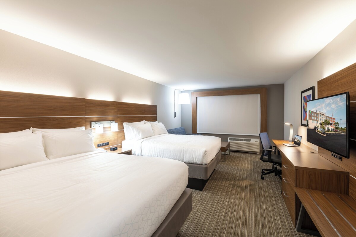 Een hotelkamer met twee bedden, een bureau met een computer, een televisie en een groot raam.