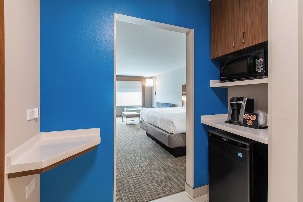 A compact hotel room with a kitchenette, a bed, and a view of the hallway.