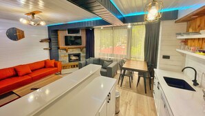 A modern kitchen with a central island, a dining area with a wooden table and chairs, a red sofa, and a TV mounted on the wall.
