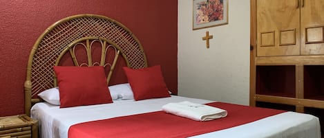 A bed with a wooden headboard, red bedding, and a white blanket.