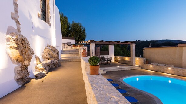 Un espace aménagé au bord de la piscine, avec un mur en pierre, des sièges d’extérieur et une vue sur le paysage environnant.