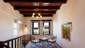 Une pièce avec un plafond en bois, une table entourée de chaises, deux fenêtres et une petite table ornée d’objets décoratifs.