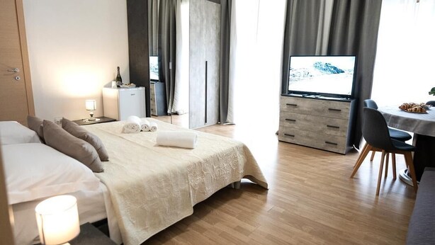 A modern hotel room with a bed, bedside table, TV, and a desk area. - Home Josèphine (Caserta)