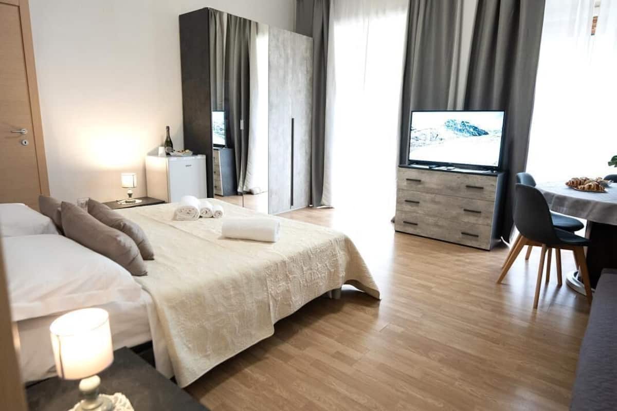 A modern hotel room with a bed, bedside table, TV, and a desk area.