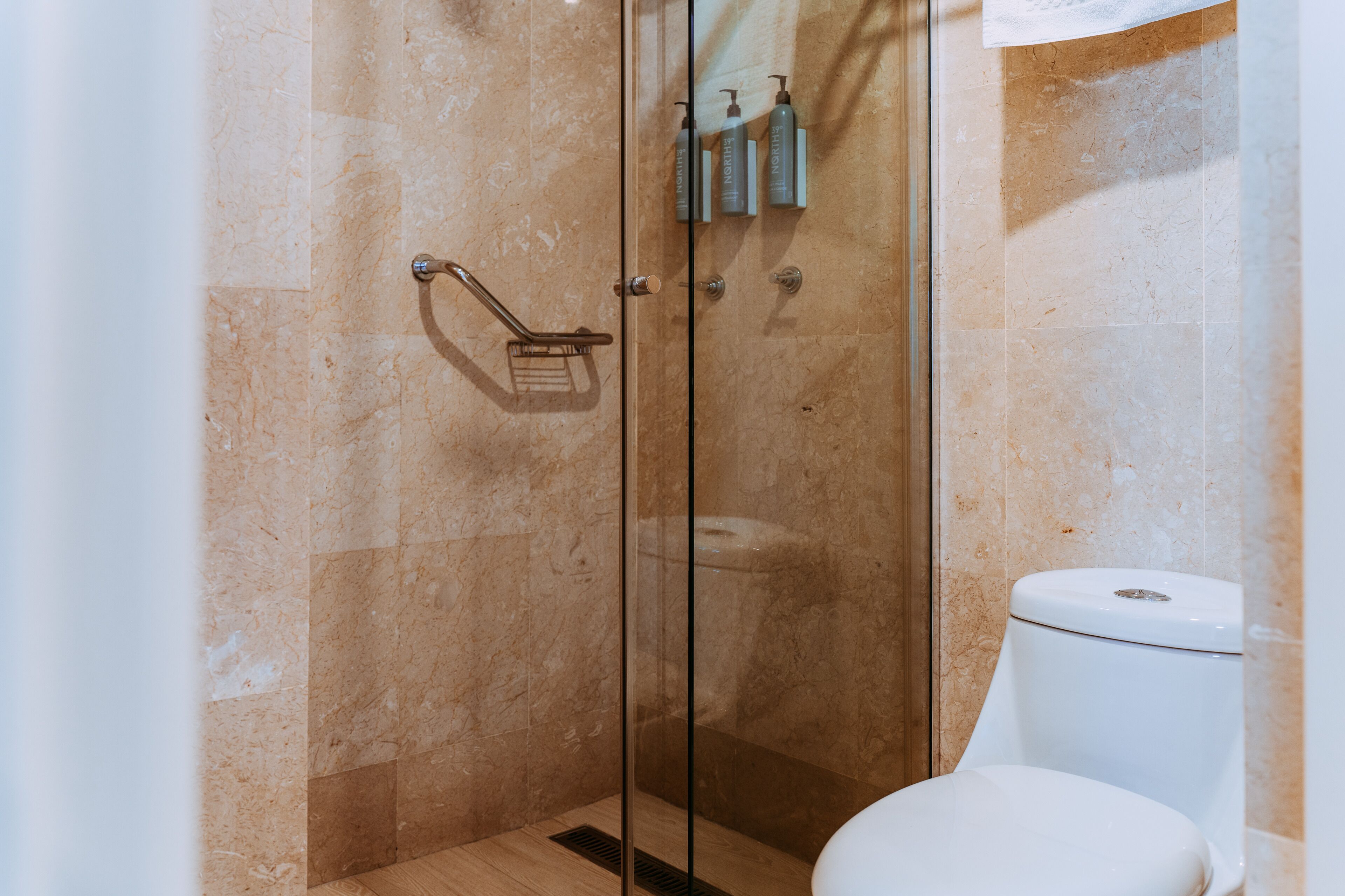 A bathroom with a glass-enclosed shower, a toilet, and toiletries on the wall.