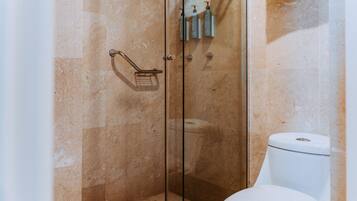 A bathroom with a glass-enclosed shower, a toilet, and toiletries on the wall.