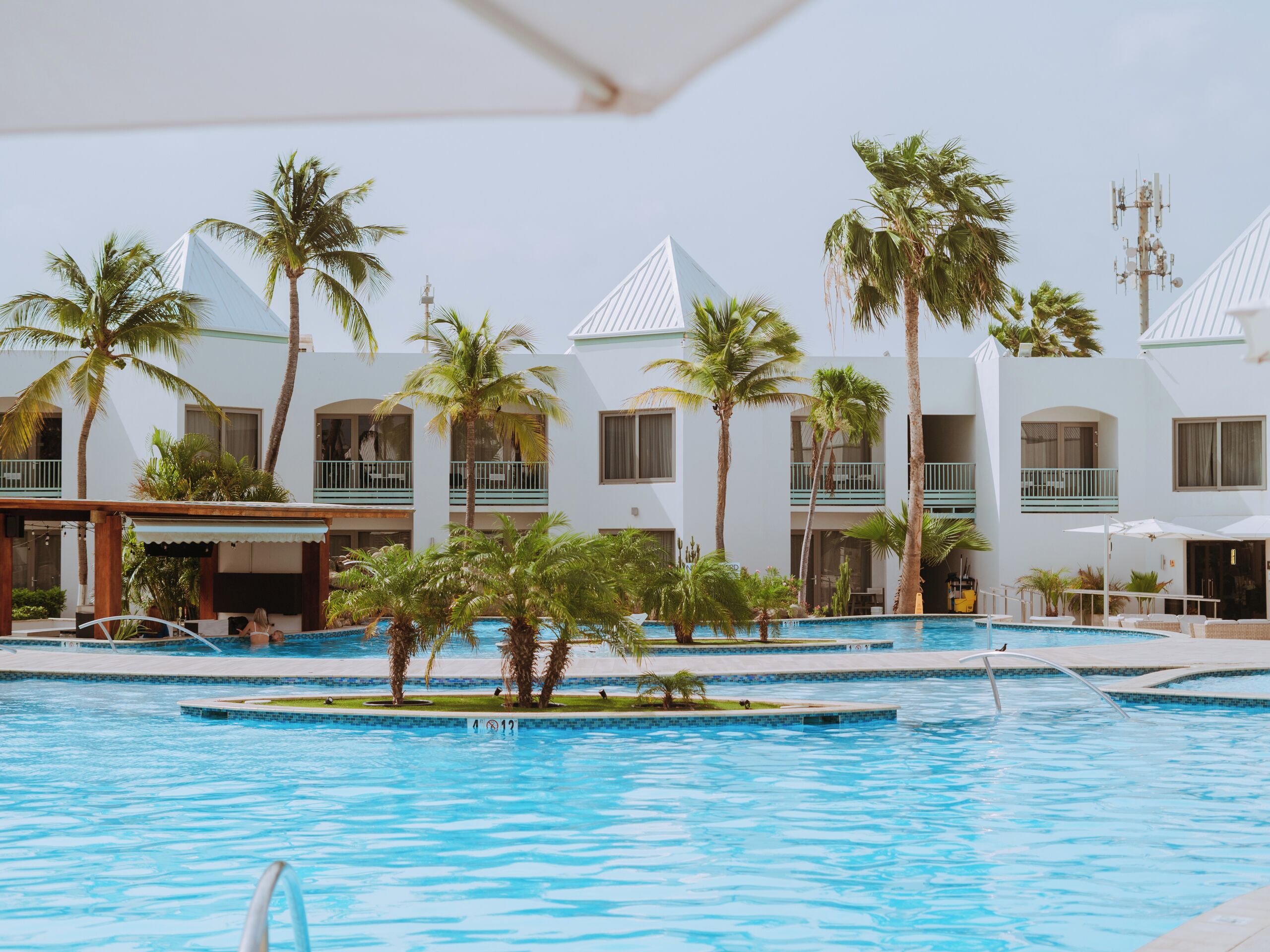 Uma área de piscina em resort com várias piscinas, palmeiras e edifícios do resort com varandas.