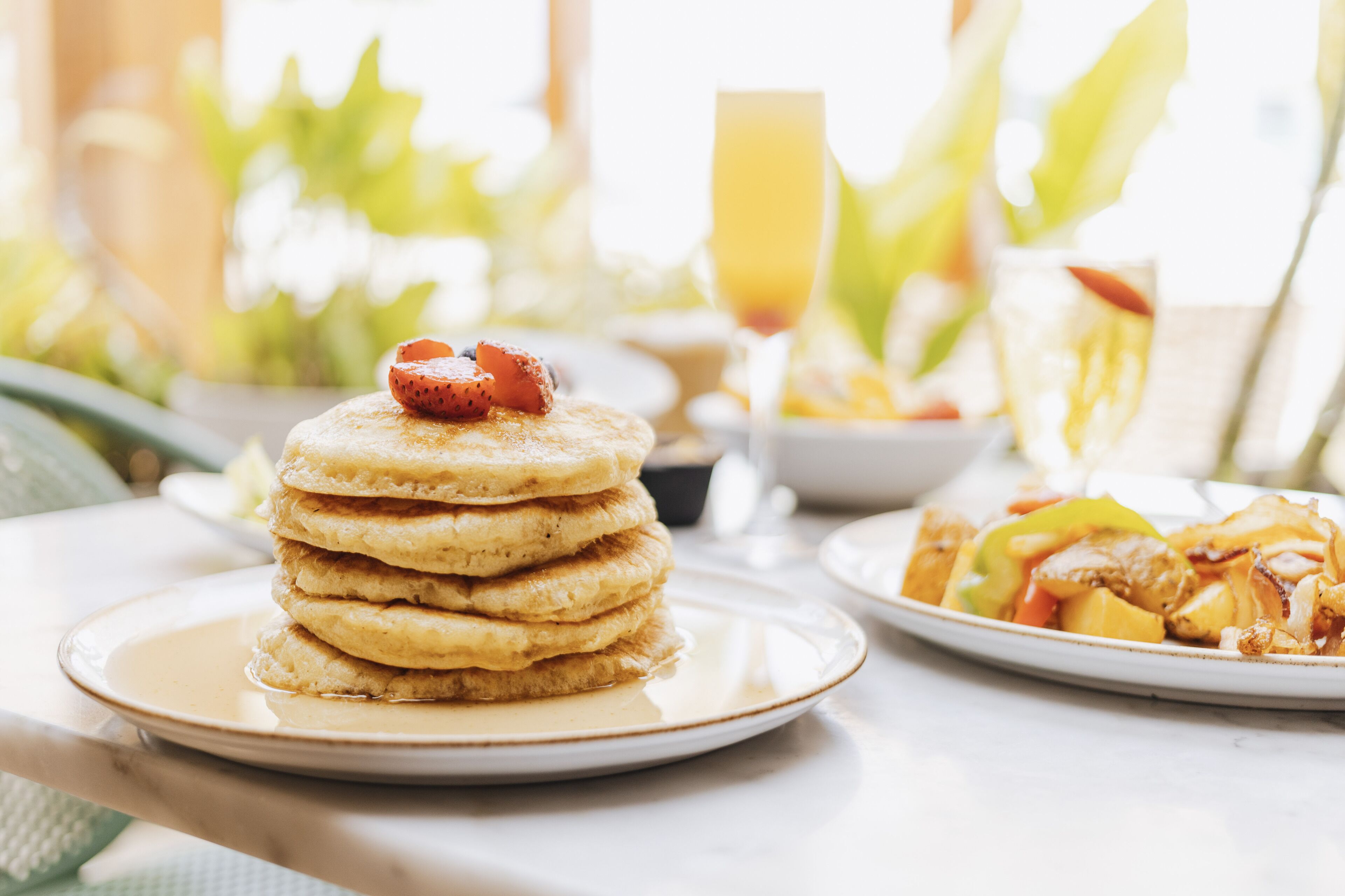 Una mesa con desayuno que incluye panqueques, fruta y un vaso de jugo de naranja.