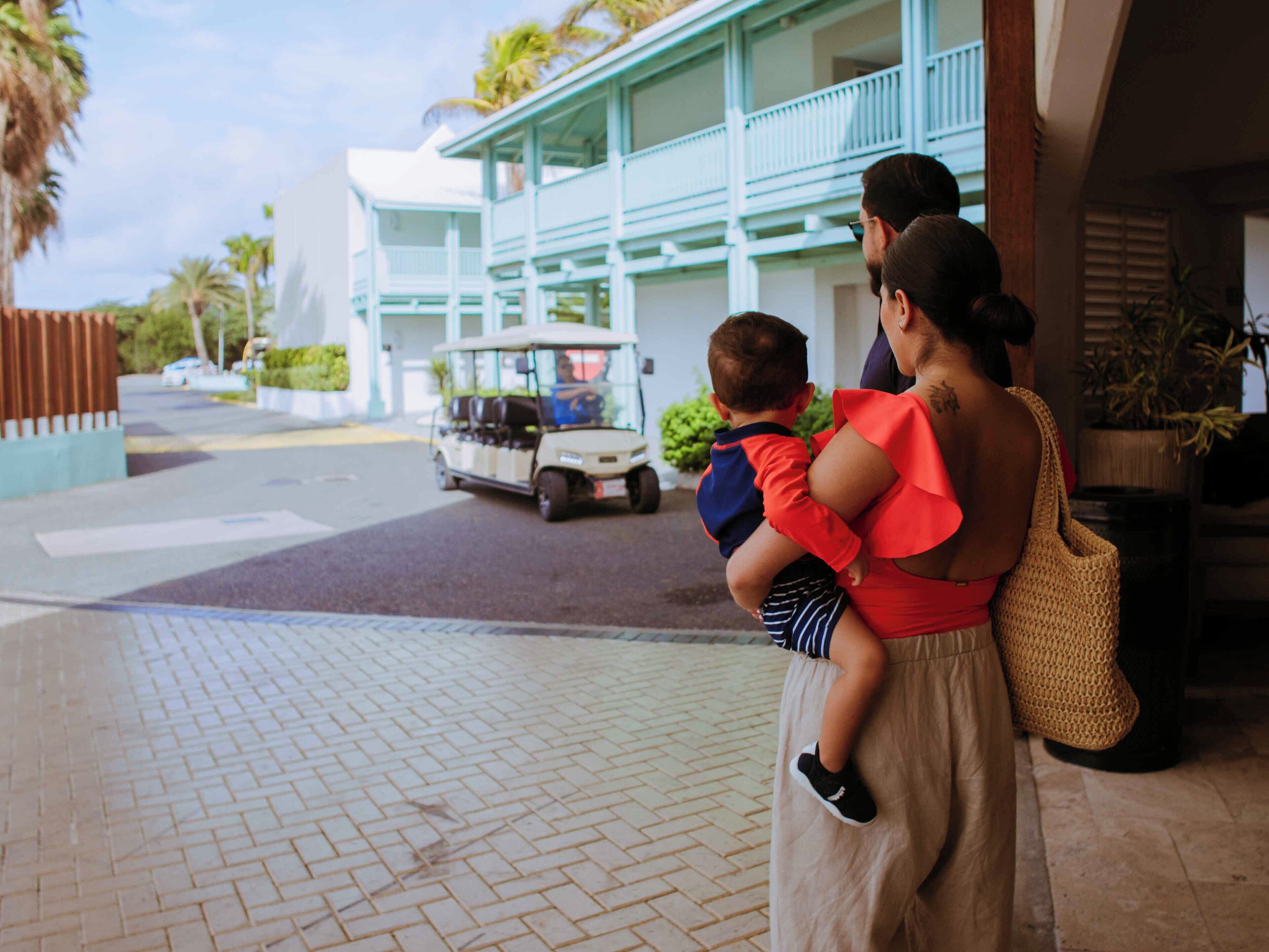 A person holding a child, standing on a paved area with a building in the background.