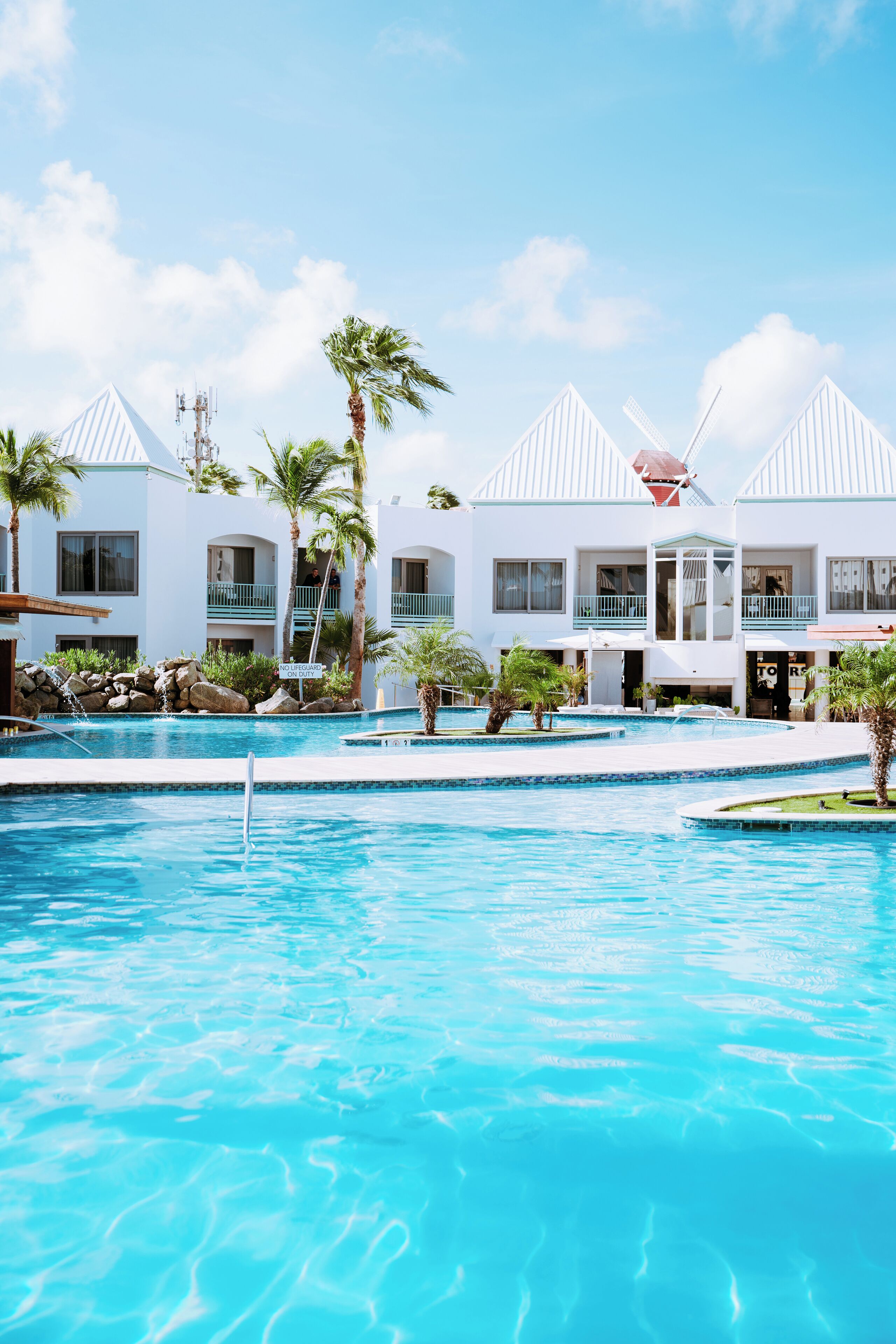 Ein Resort mit Schwimmbad, Palmen und weißen Gebäuden mit Balkonen.