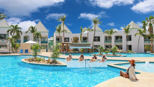 Un área de piscina en un resort, con varias piscinas, palmeras y sillas de descanso.