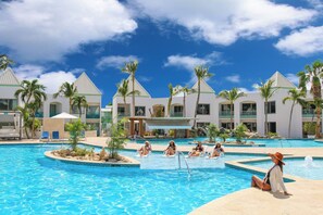 Un área de piscina en un resort, con varias piscinas, palmeras y sillas de descanso.