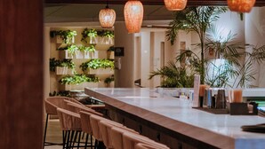 Zona de bar moderna con una barra larga, varios taburetes e iluminación colgante.