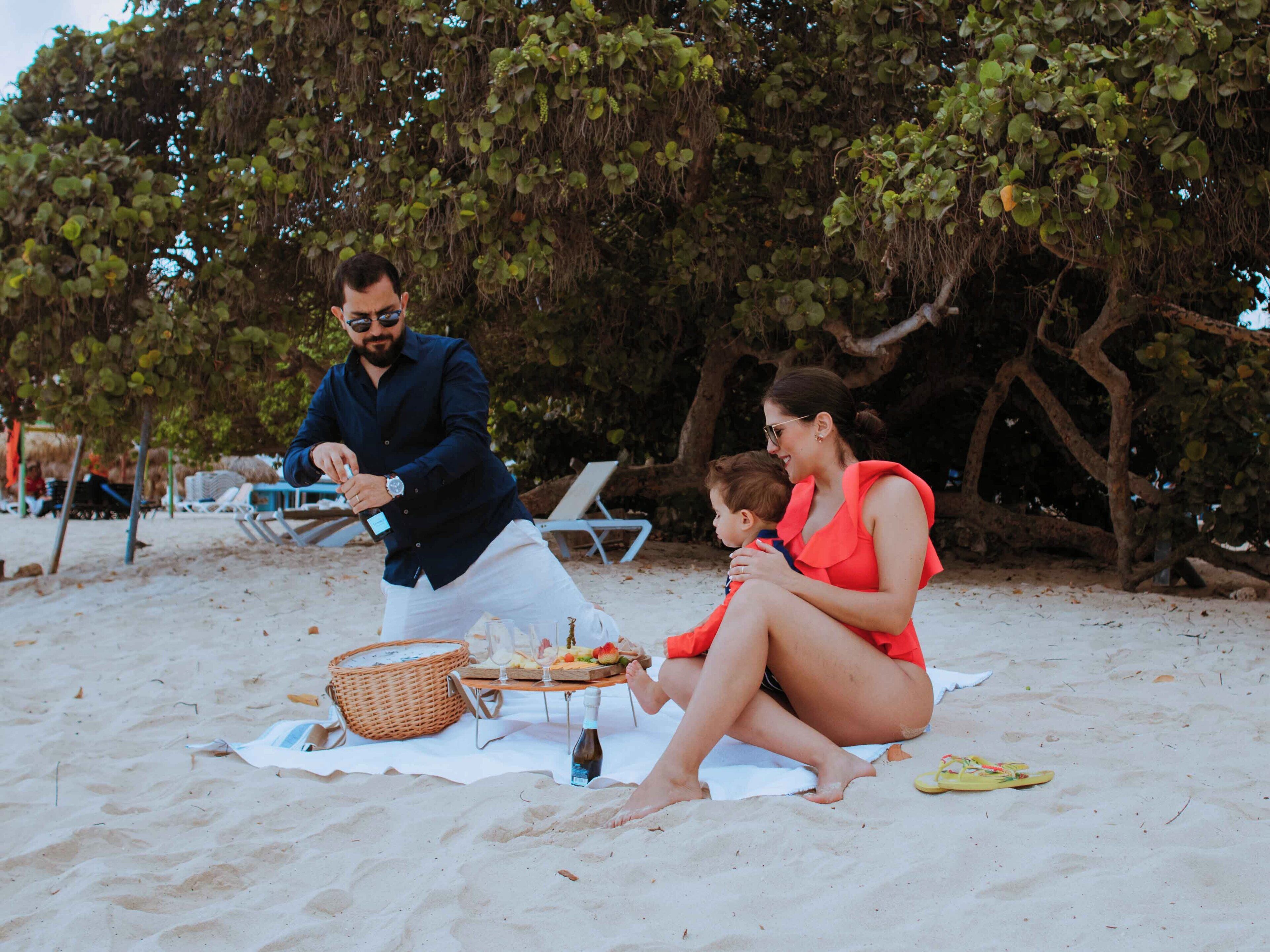 A beach scene with a picnic setup including a basket, food, and drinks.