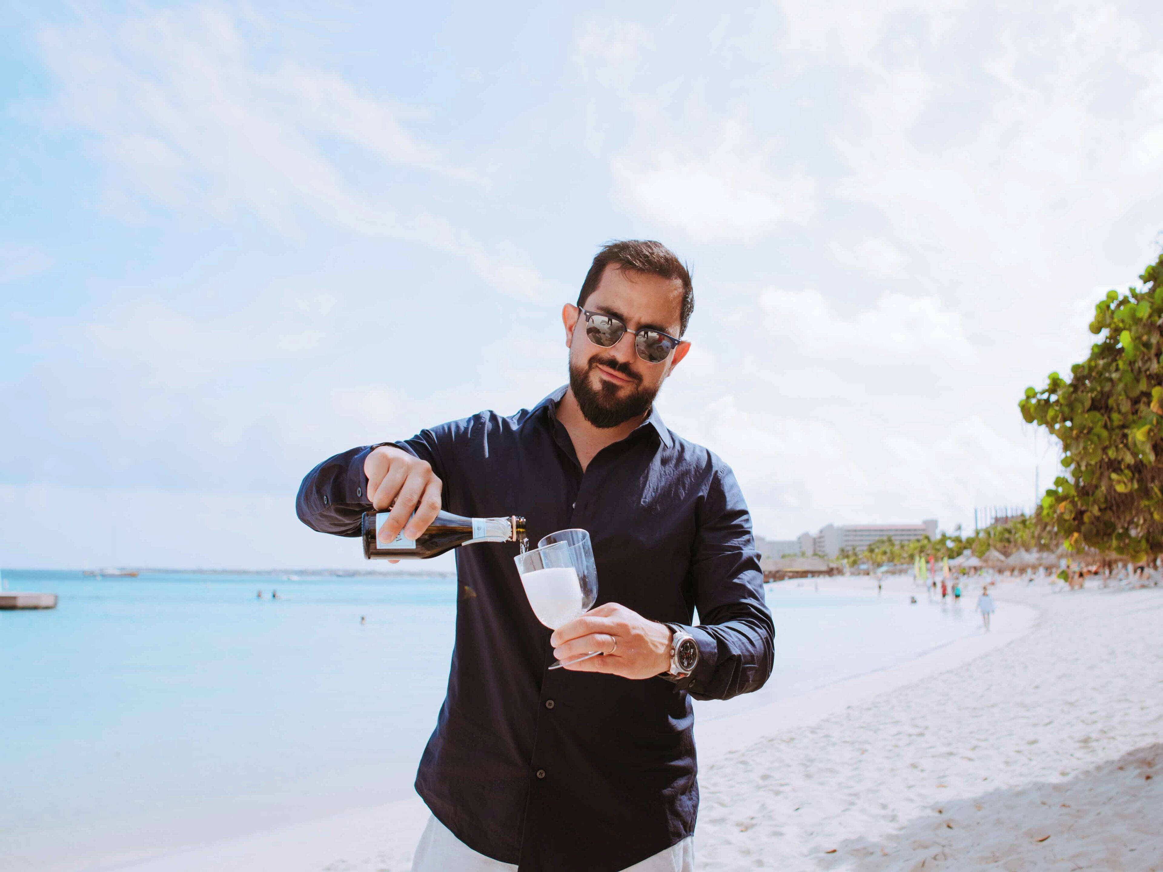 A man pouring a drink into a glass on a beach.