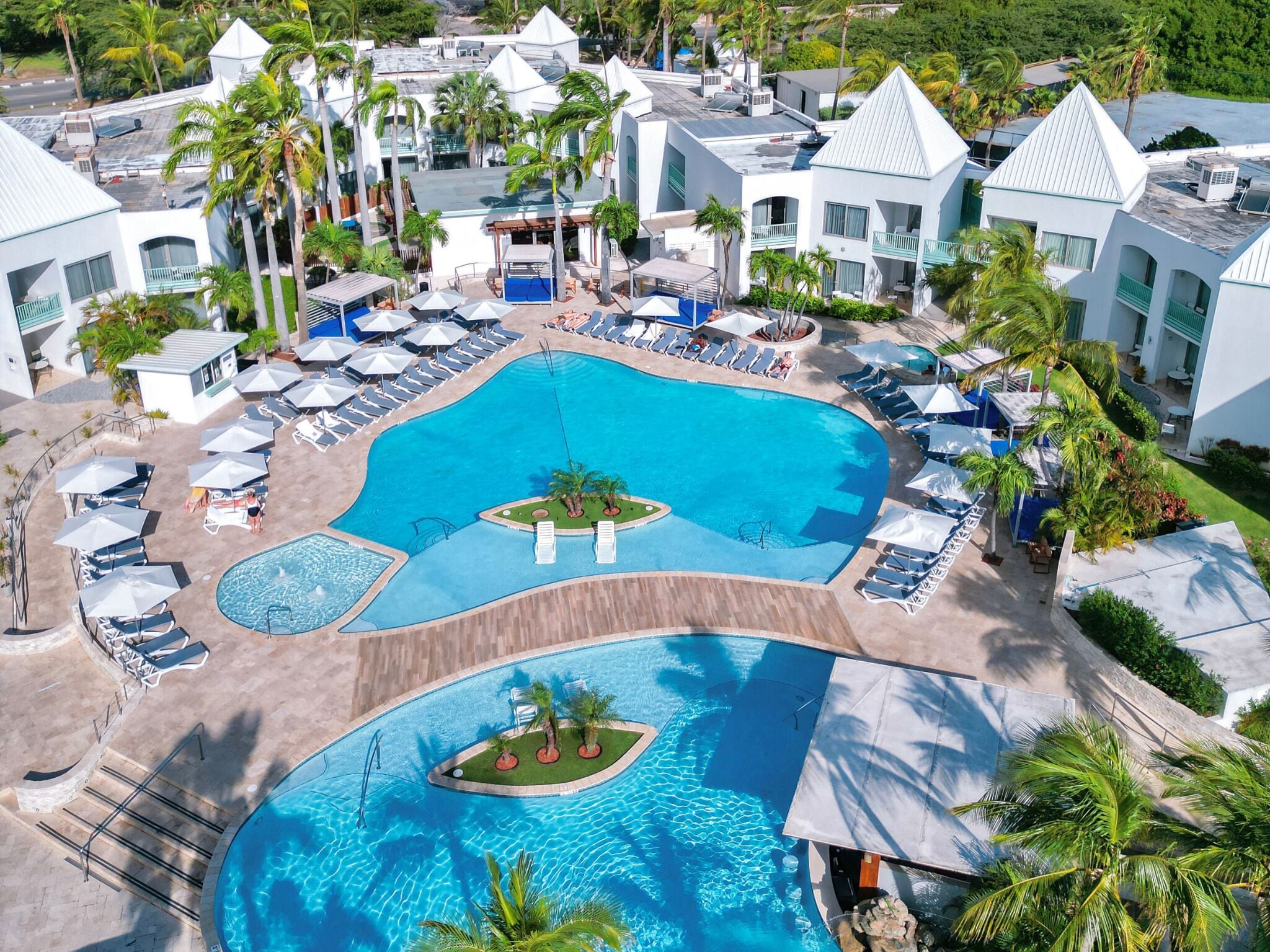 Ein Resort mit mehreren Schwimmbecken, Liegestühlen und Palmen.